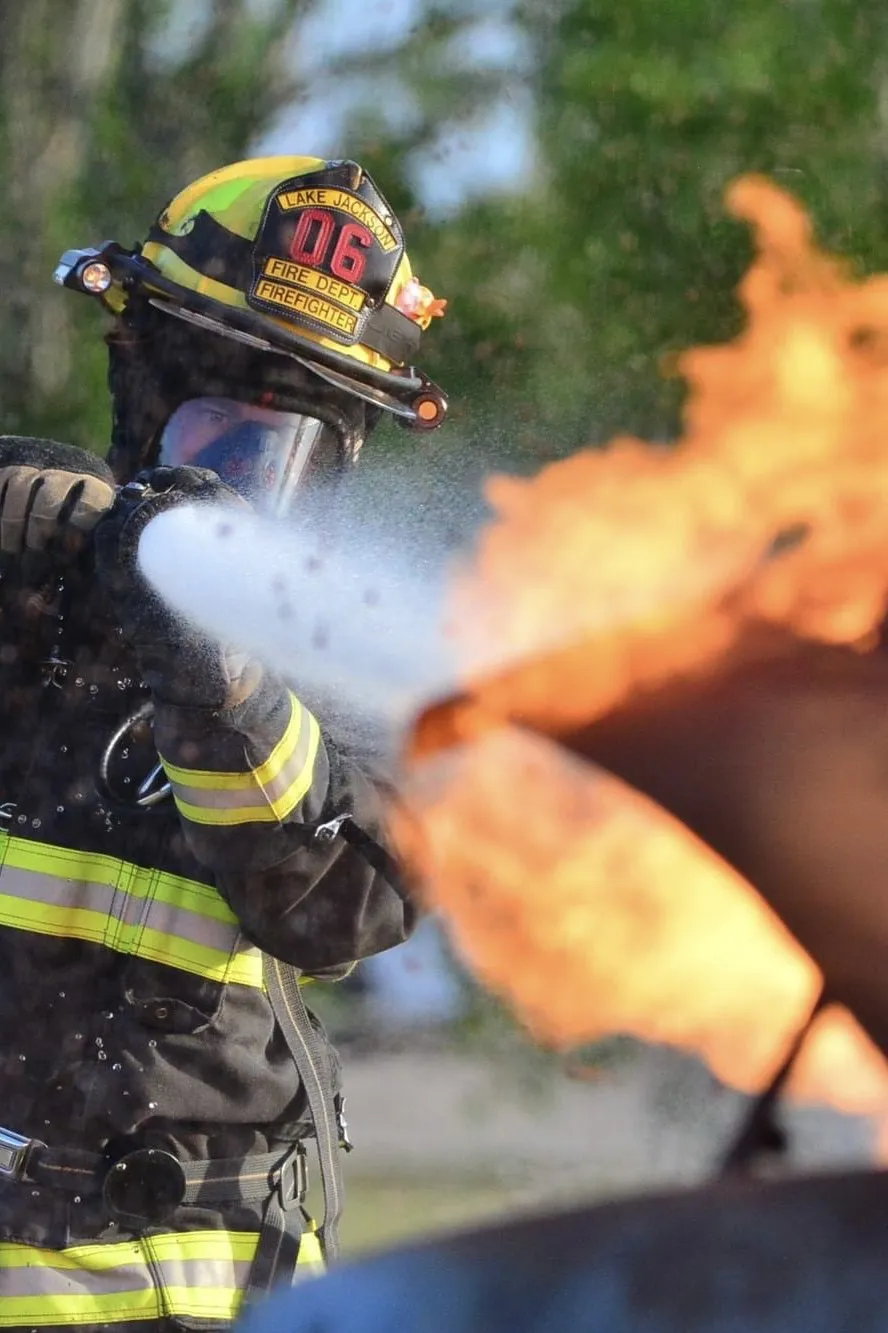 Brandon in full firefighting gear on the nozzle, water hitting a fire
